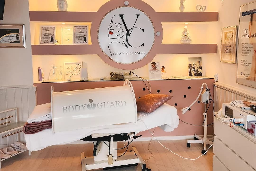Behandlungsraum mit Liege, Wärmehaube und dem Vlera-Cosmetics-Logo an der Wand